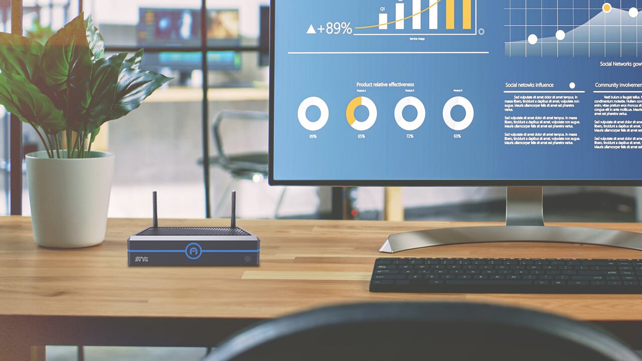 A modern workspace featuring a computer monitor displaying graphs related to data security, with a mini PC in the foreground and a plant beside it.