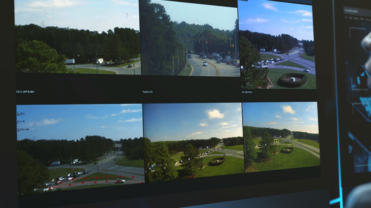 A multi-screen display powered by the CORTROL Video Wall System shows various traffic camera feeds of intersections surrounded by trees and vehicles in a residential area on a sunny day.